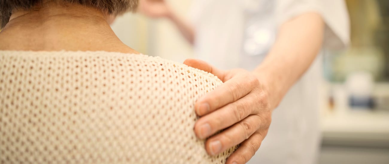 Sjukvårdspersonal håller handen på ryggen på äldre kvinna.