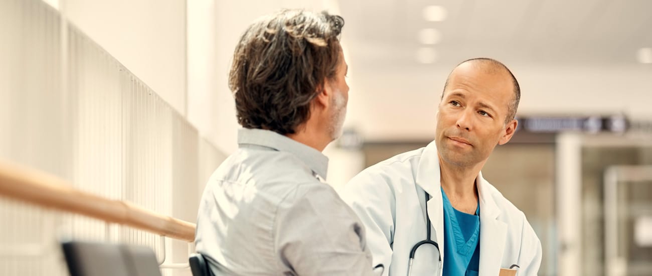 Manlig läkare samtalar med man i sjukhusmiljö.